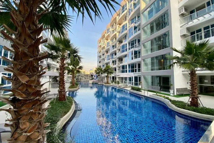 Grand Avenue Residence large swimming pool with water slide, rock waterfall, and palm trees surrounded by condo buildings.