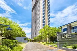 Unixx South Pattaya tall condo building exterior with entrance gate, lush greenery, and property sign on a sunny day.