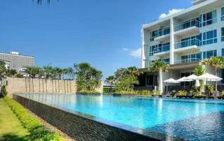 Cetus Beachfront large outdoor swimming pool with a modern white building and palm trees under a blue sky.
