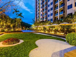 Unixx South Pattaya outdoor swimming pool area at dusk with illuminated landscaping, lounge chairs, and tall building.