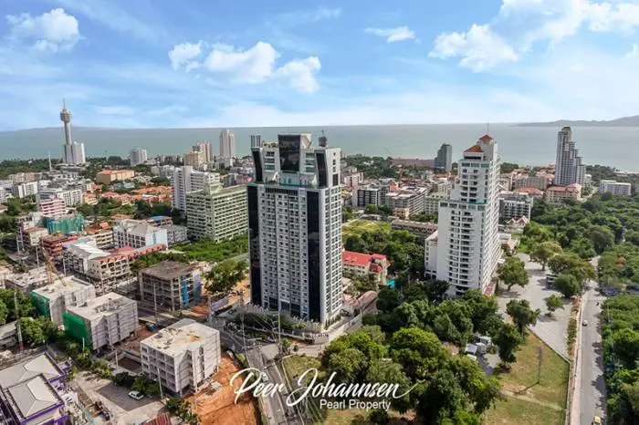 The Vision: Aerial view of Pattaya cityscape with high-rise buildings, ocean, and distant mountains under a blue sky.