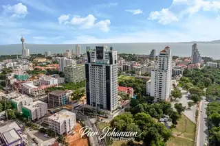 The Vision: Aerial view of Pattaya cityscape with high-rise buildings, ocean, and distant mountains under a blue sky.