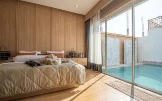 Narita Villa bedroom with a large bed, wood paneling, and sliding glass doors opening to a private pool.