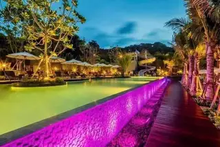 Unixx South Pattaya main swimming pool with vibrant purple LED lighting along the edge and illuminated palm trees at night.
