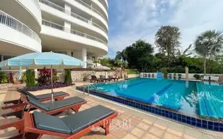 Baan Rimpha large curved swimming pool with ocean view, sun loungers, and white buildings on a sunny day.