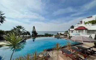 Baan Rimpha infinity pool with ocean view, sun loungers, and a striped umbrella under a bright sky.