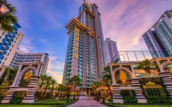 Riviera Monaco high-rise condo building with illuminated signage, surrounded by lush landscaping and decorative entryways at sunset.