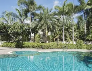 The Meadows large swimming pool with reflections of the clubhouse and tropical trees under a sunny sky.