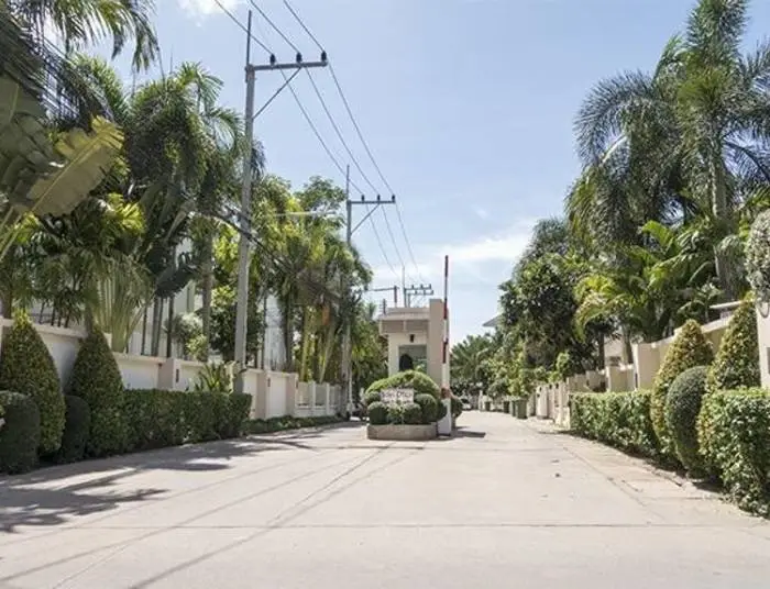 The Meadows gated community entrance with security barrier, lush palm trees, and manicured hedges.