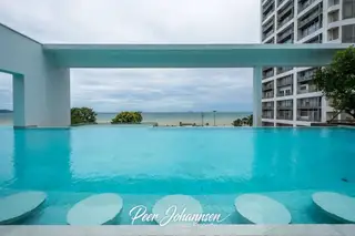 Aeras swimming pool with underwater bar stools and an ocean view under a cloudy sky.