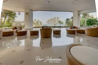 The Cove Pattaya outdoor lounge area with woven furniture and a view of the ocean and palm trees.