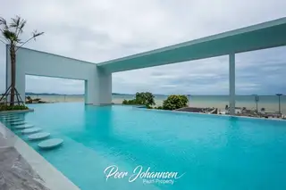 Aeras infinity pool with steps, palm trees, and a wide ocean view under a cloudy sky.