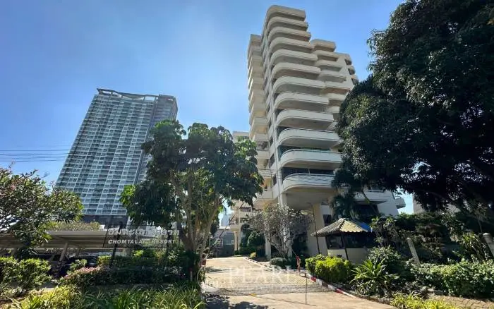Chom Talay Resort exterior, showing the main building with curved balconies, lush trees, and a modern high-rise in the background.