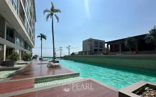 Musselana swimming pool with wooden deck, palm trees, and the condo building on a sunny day.