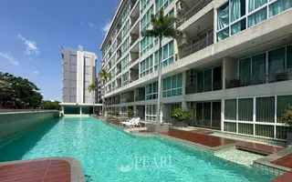 Musselana long swimming pool with sun loungers, wooden decking, and the modern condo building facade.