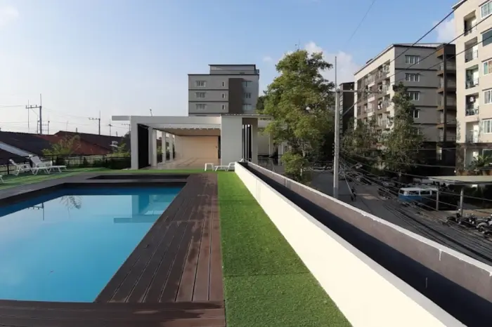 The Mountain Eakmongkol rooftop swimming pool with wooden deck, artificial grass, and surrounding buildings.