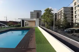 The Mountain Eakmongkol rooftop swimming pool with wooden deck, artificial grass, and surrounding buildings.