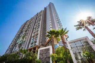 The Riviera Jomtien upward angle view of the tall, modern building facade with palm trees and decorative screens in the foreground.