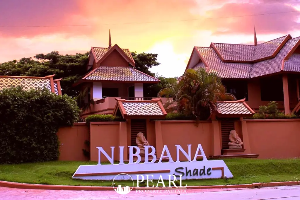 Nibbana Shade entrance sign with traditional Thai-style buildings under a vibrant sunset sky.