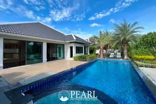 European Thai House exterior with large swimming pool, wooden deck, and palm trees under a blue sky.