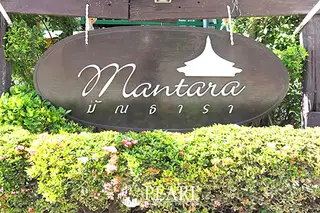 Mantara Village entrance sign with ornate script and a temple-like silhouette, surrounded by lush green foliage.