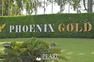 Phoenix Gold Golf entrance sign with golden letters on a green hedge, surrounded by lush grass and foliage.