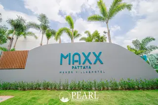 Maxx Pattaya entrance sign with "MAXX PATTAYA MANOR VILLA & HOTEL" lettering, palm trees, and green grass.
