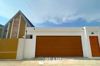 Baan Mae 2 Villa front exterior with two brown garage doors, dark entrance door, and white walls under a cloudy sky.