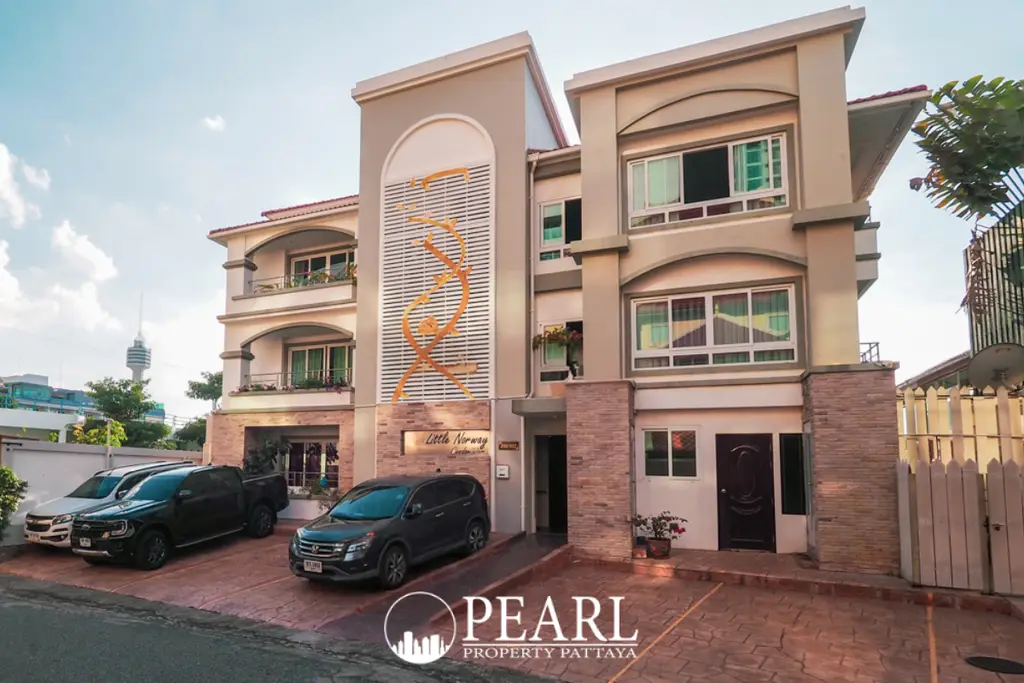 Little Norway Condominium exterior view of the building with parked cars and a Pattaya city tower in the background.