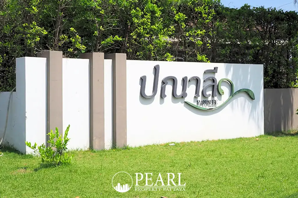 Baan Panalee entrance sign in Thai and English on a white wall with green grass and foliage.