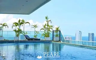 Cosy Beach View rooftop infinity pool with lounge chair, palm trees, and panoramic ocean and city views under blue sky