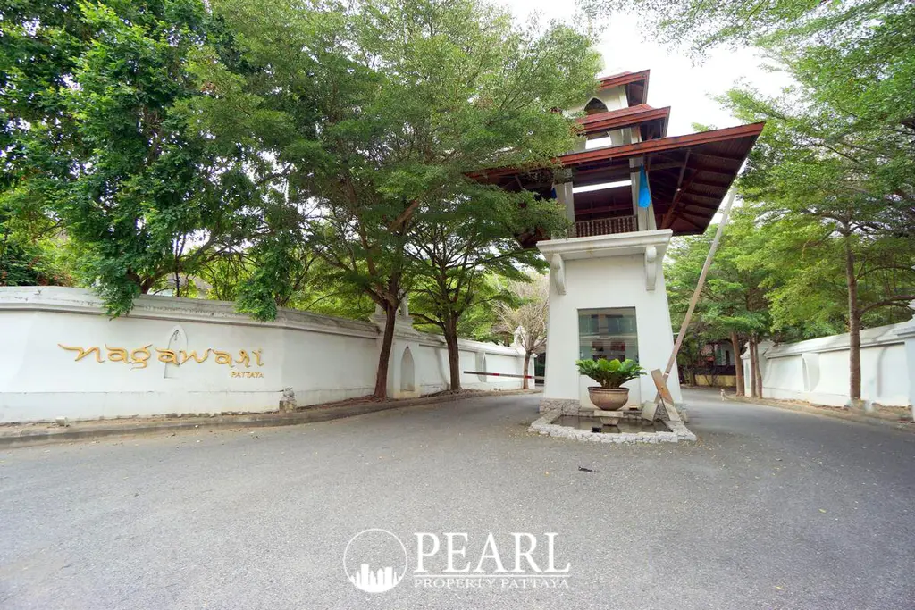 Nagawari Pattaya main entrance gate with white wall, gold lettering, traditional Thai-style security booth, and lush green trees.