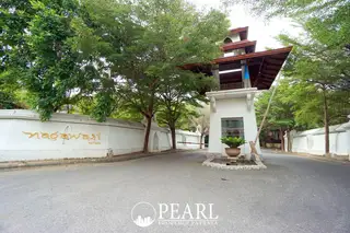 Nagawari Pattaya main entrance gate with white wall, gold lettering, traditional Thai-style security booth, and lush green trees.