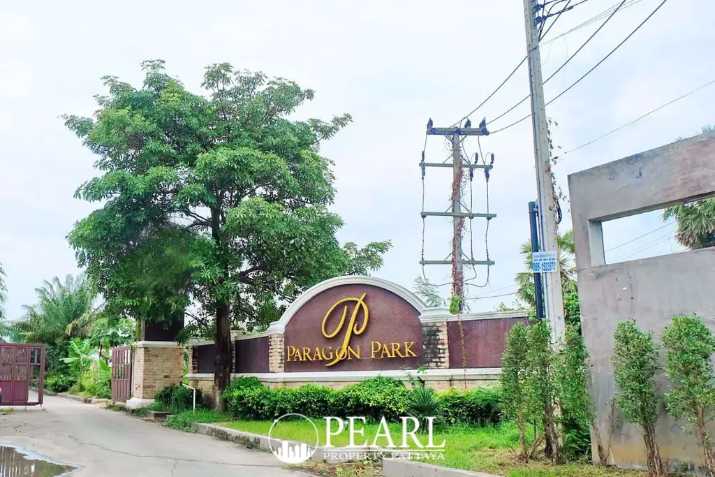 Paragon Park Village entrance sign with golden letters, surrounded by green foliage and a large tree.