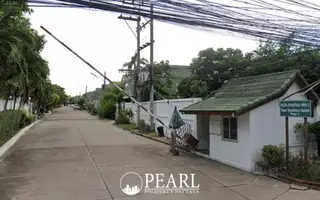 Baan Suan Suwattana Phase 2 entrance gate with security booth and barrier, leading to a residential street.