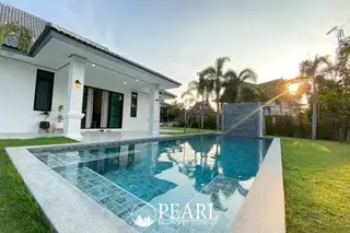 The Lanterns outdoor swimming pool with a water feature, green lawn, and a modern house at sunset.