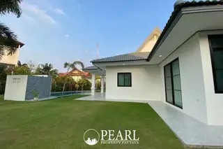 The Lanterns outdoor swimming pool with a water feature, green lawn, and a modern house at sunset.