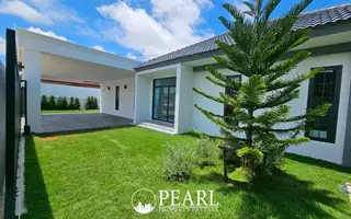 Hillside Village Pattaya modern house exterior with a large green lawn, covered carport, and a young pine tree.