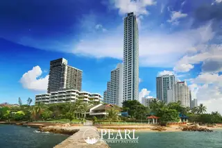 Sliver Beach condo buildings on the Pattaya coastline, with a stone pier extending into the ocean under a bright blue sky.