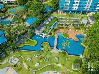 Palm Wongamat aerial view of a large, blue swimming pool with a bridge, surrounded by green lawns, palm trees, and sun loungers.