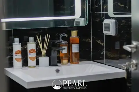 1 Bedroom Condo for Sale at Grand Solaire Pattaya: Bathroom vanity with white sink, black faucet, and various toiletries.