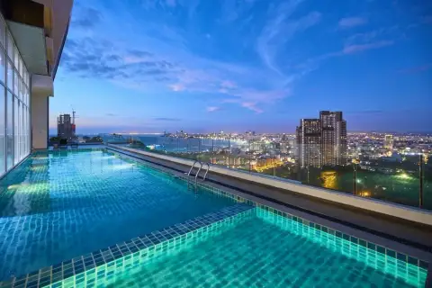 The Vision: Rooftop infinity pool at dusk, reflecting city lights and the illuminated Pattaya skyline.