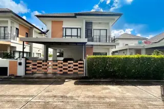 Patta Village modern two-story house exterior with carport, patterned gate, green hedge, and blue sky.
