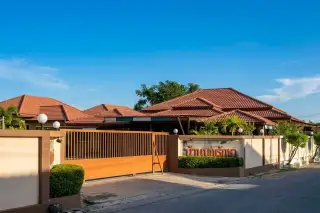 Baan Boon Raksa main entrance with orange gate, sign, and red-tiled roofs of the buildings in Pattaya.