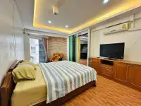 1 Bedroom Condo for Sale at Rimhad Jomtien Condominium bedroom with striped bedding, wood cabinetry, and flat-screen TV