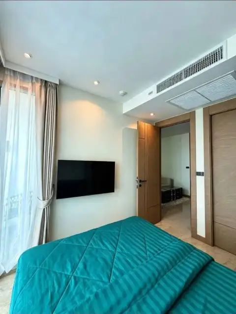 1 Bedroom Condo for Rent at Riviera Ocean Drive bedroom with teal bedding, wall-mounted TV, and sheer curtains