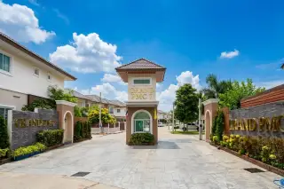 Grand PMC 7 main entrance with security booth, barrier gate, and residential buildings under a blue sky.