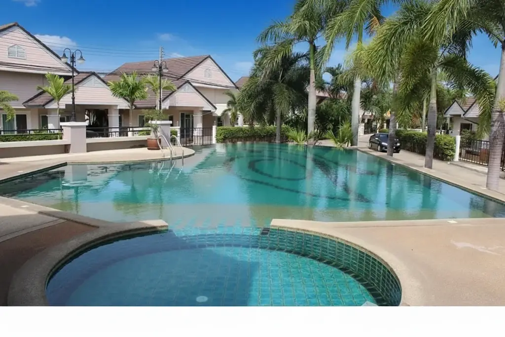 Ruen Pisa Village large swimming pool with a circular spa, surrounded by palm trees and village houses in the background.