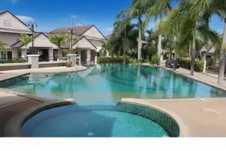 Ruen Pisa Village large swimming pool with a circular spa, surrounded by palm trees and village houses in the background.