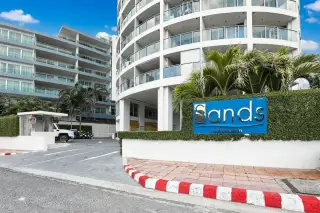 Sands Condominium main entrance with a blue sign featuring the property name, surrounded by green hedges.